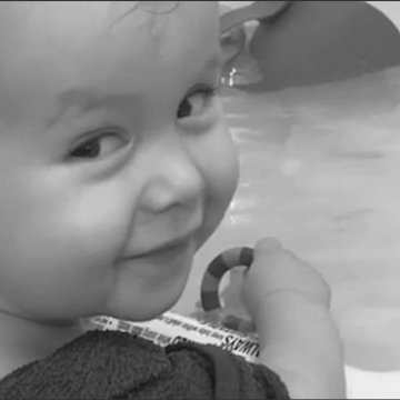 Owen age 1 years old smiling looking behind his shoulder in the bath playing with a toy