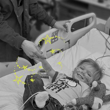 Nurse holding Zach's hand (age) as he's smiling in a hospital bed
