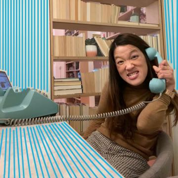 A young woman sits at a desk on the phone smiling. Blue doodles surround her.